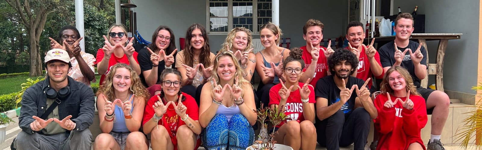 Two rows of students wearing red shirts make "W"s with their hands. 